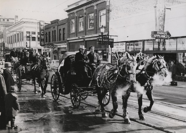 photograph of a parade with wagons pulled by horses